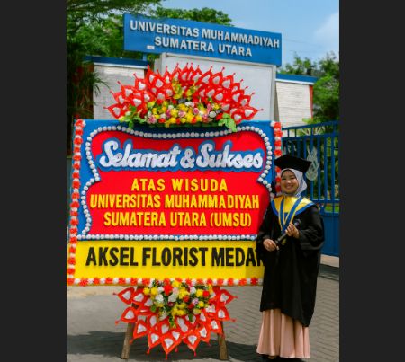 Karangan bunga ucapan selamat wisuda Universitas Muhammadiyah Sumatera Utara (UMSU) dari Aksel Florist Medan, dengan latar belakang gerbang kampus dan wisudawati berpose mengenakan toga